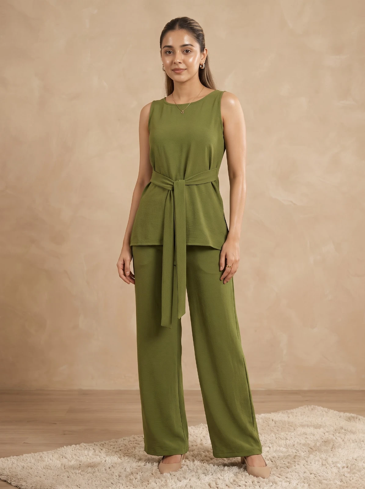 Model seated in cream armchair wearing olive sleeveless belted top and matching wide-leg pants