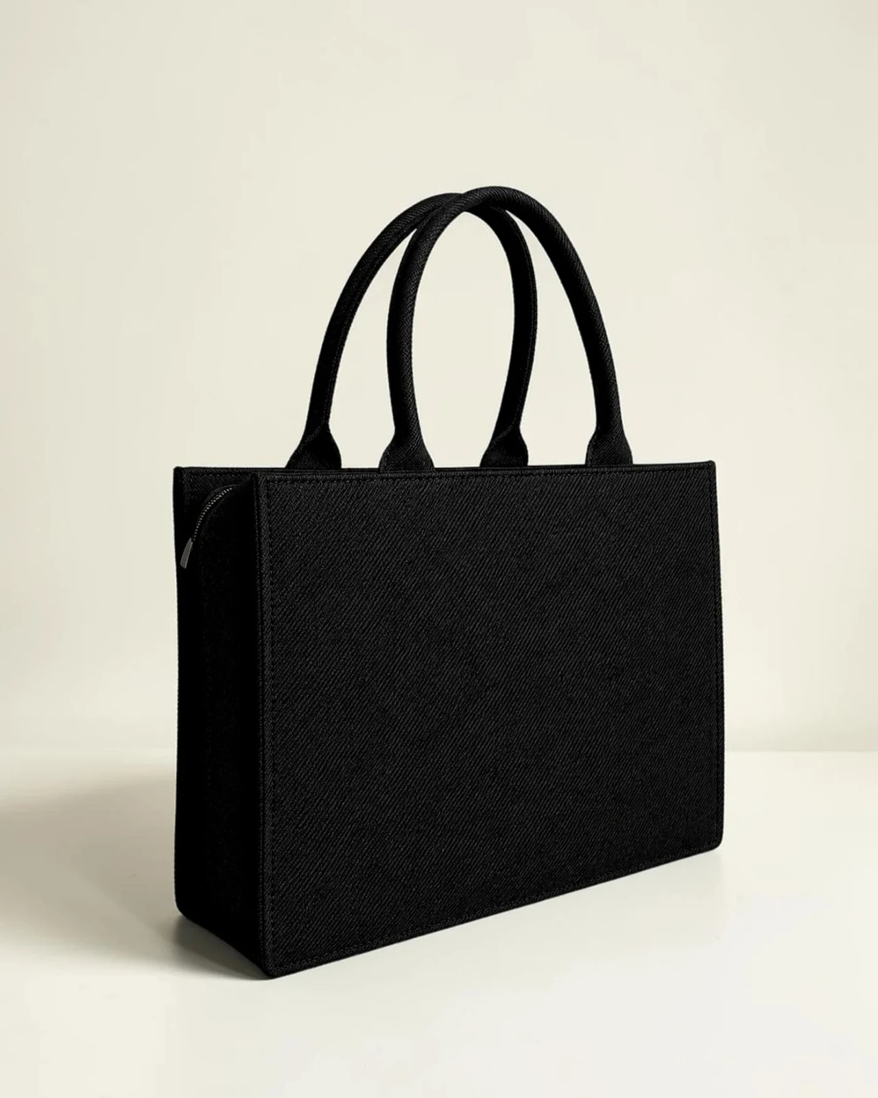 Plain black tote shown from a three-quarter side angle, highlighting structure, depth, and zipper top
