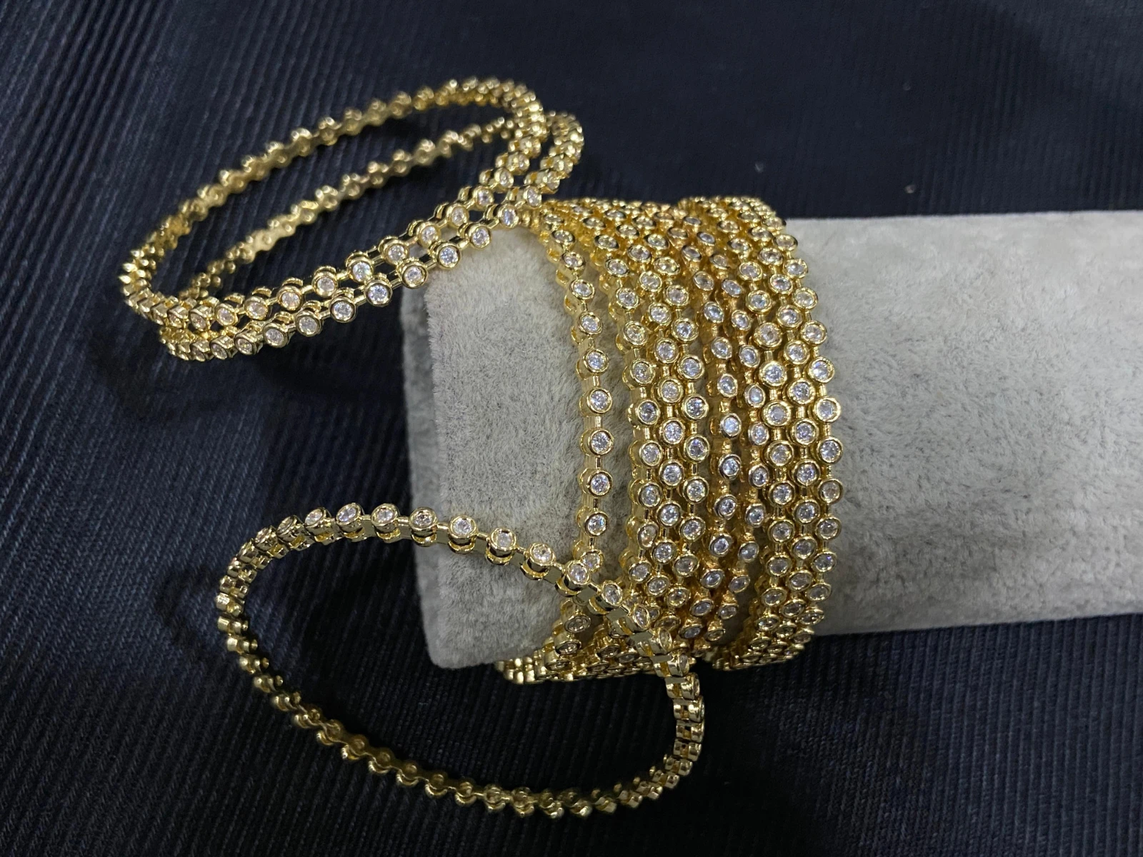 Gold-tone crystal wrap bracelet loosely looped around a gray display roll, with trailing rows against black fabric
