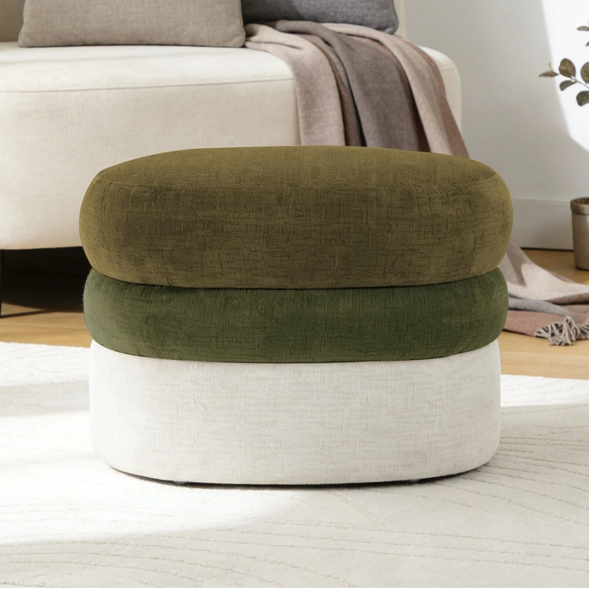 Front view of the three-tier upholstered ottoman placed on a light rug near a sofa