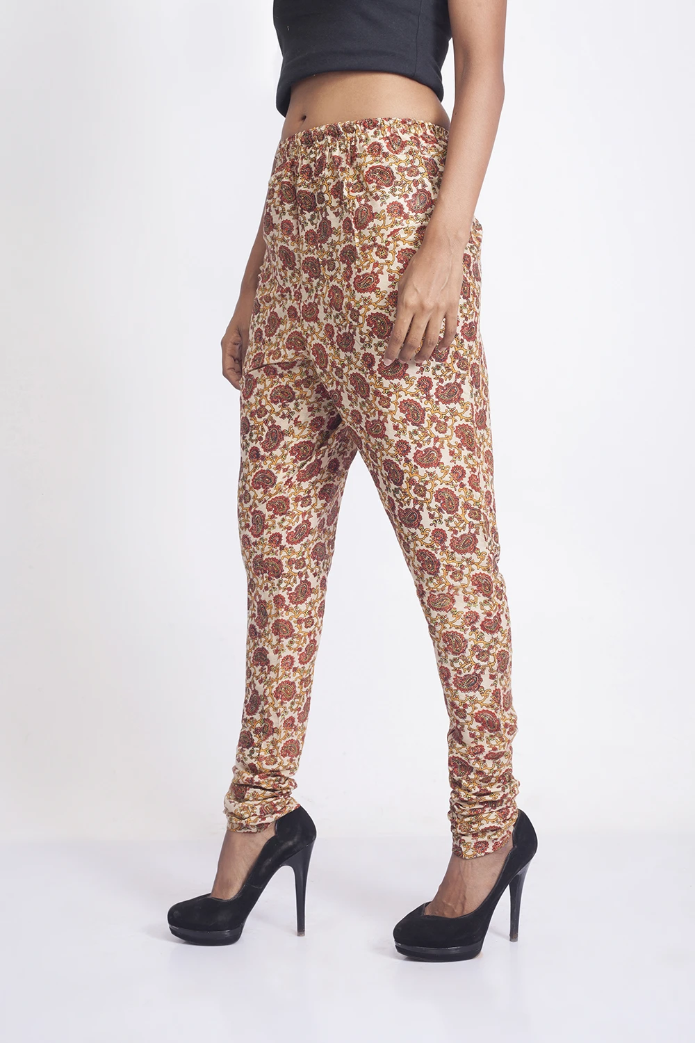 Three-quarter angled view of cream paisley leggings with elastic waist and ruched ankles, styled with black heels