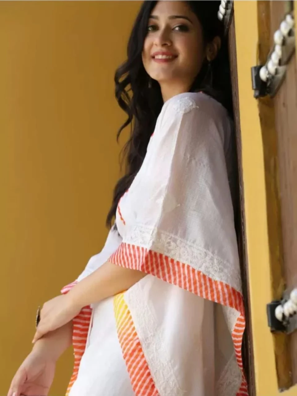 Front angled view of white kaftan kurta with drawstring waist and orange-yellow striped hem and sleeve trim