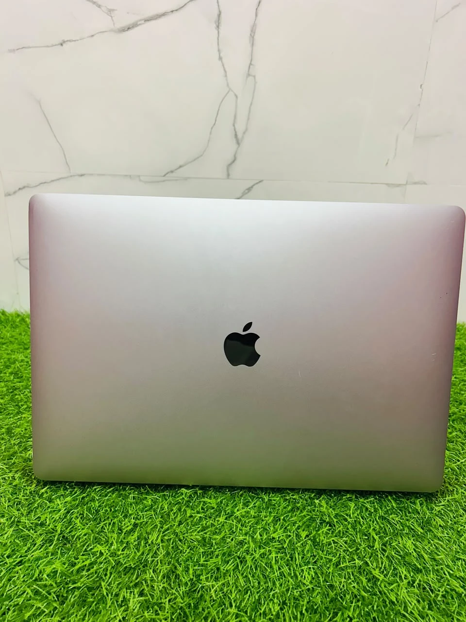 Front view of a space gray MacBook Pro open on artificial grass with the display turned on