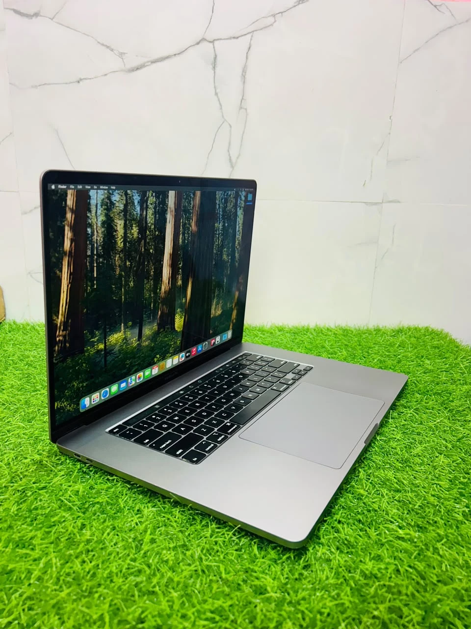 Front view of a space gray MacBook Pro open on artificial grass with the display turned on