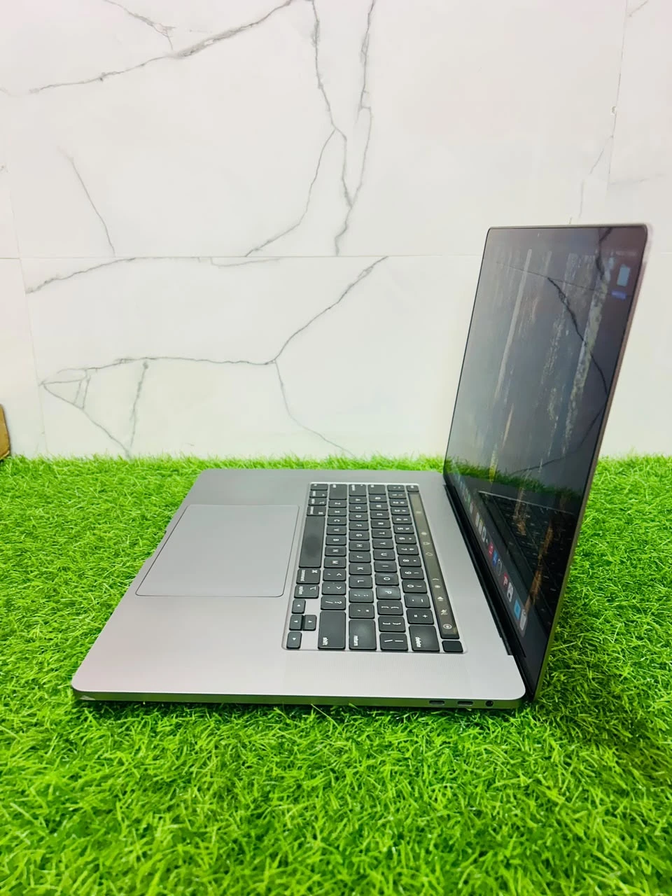 Front view of a space gray MacBook Pro open on artificial grass with the display turned on