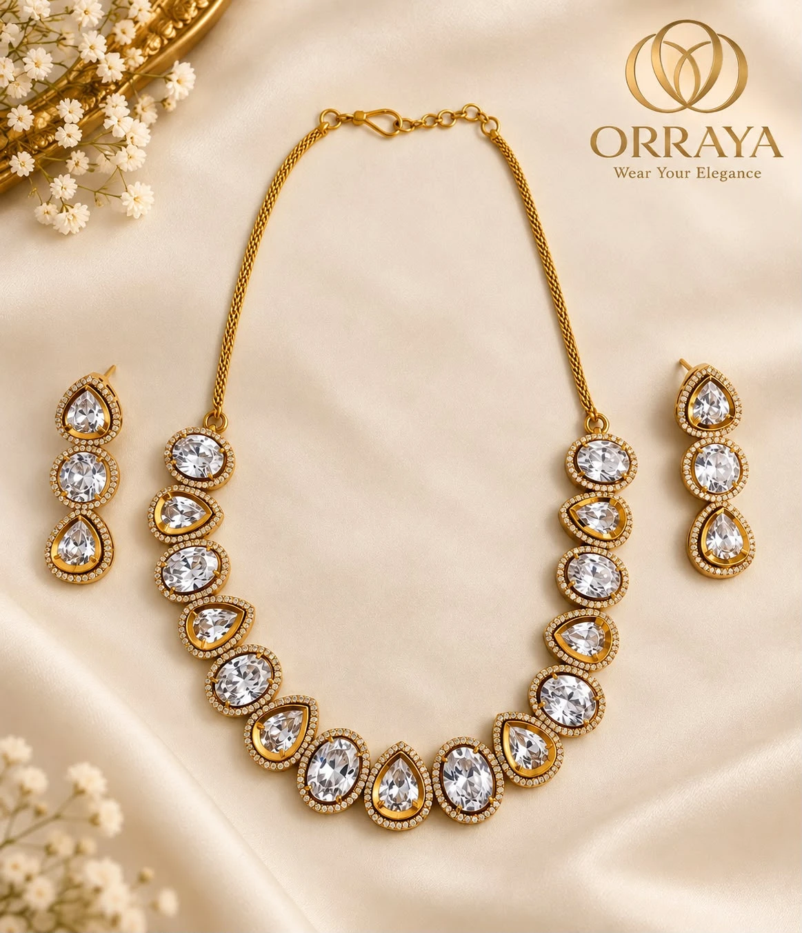 Gold-tone necklace set with clear oval and teardrop stones, paired with matching drop earrings on cream fabric