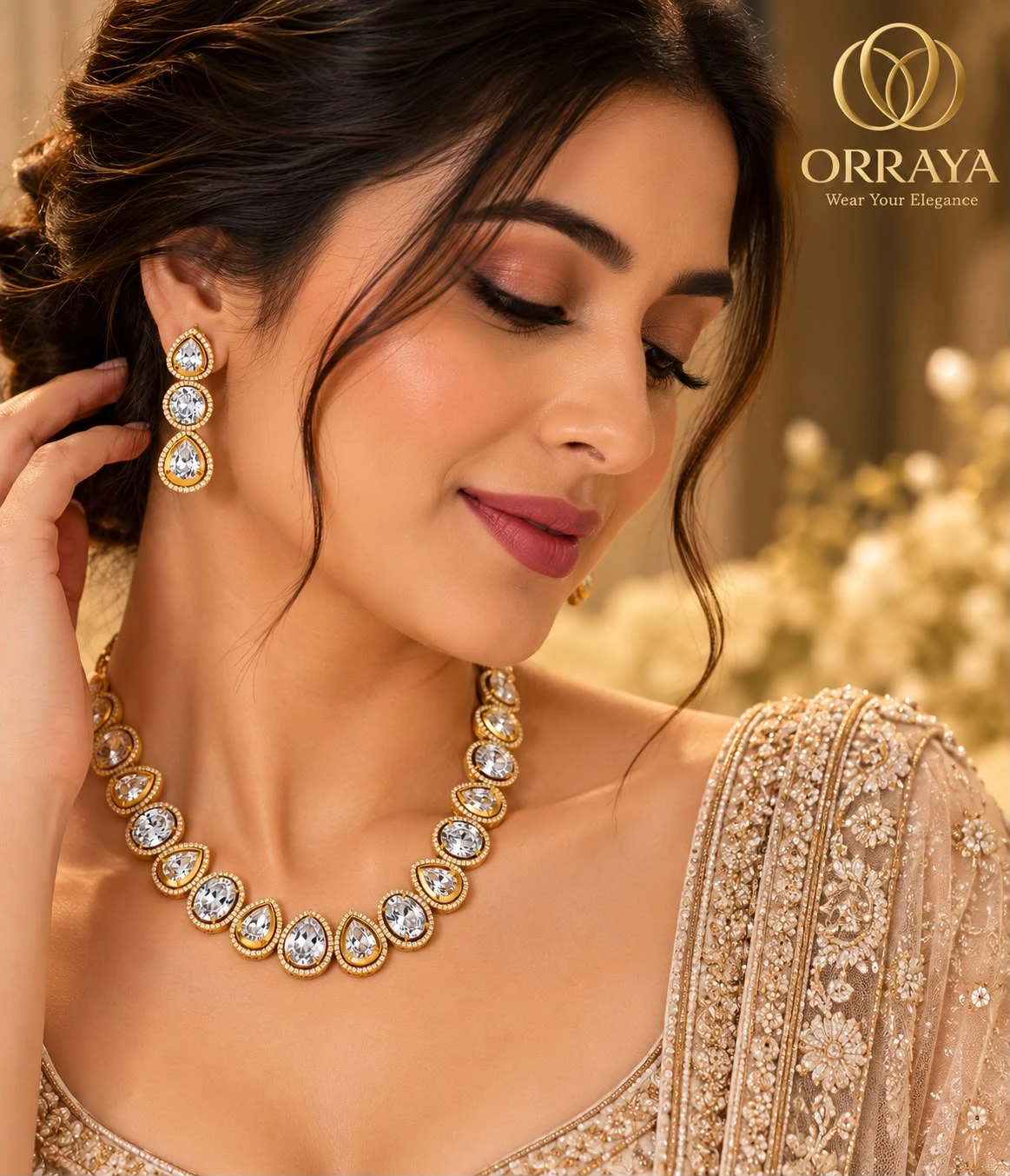Model wearing gold-tone necklace and triple-drop earrings with clear pear and round stones, Orraya logo at top right