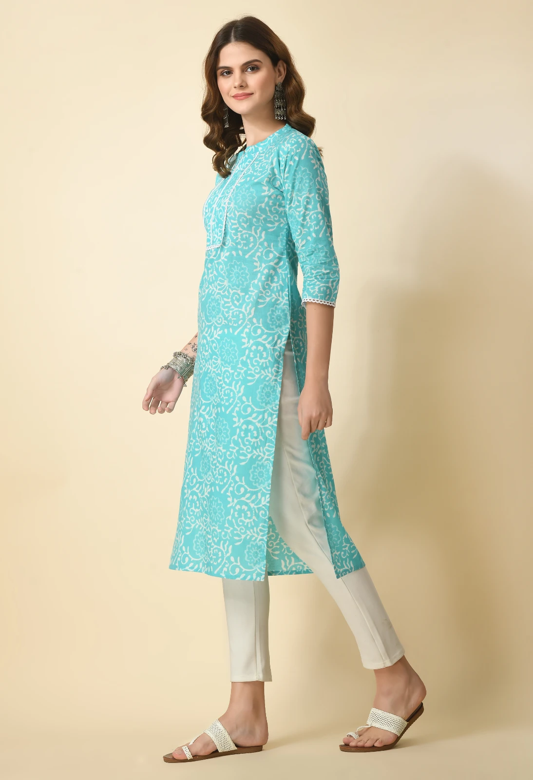 Three-quarter side view of turquoise floral kurta showing long side slit, white pants and lace-trim cuffs