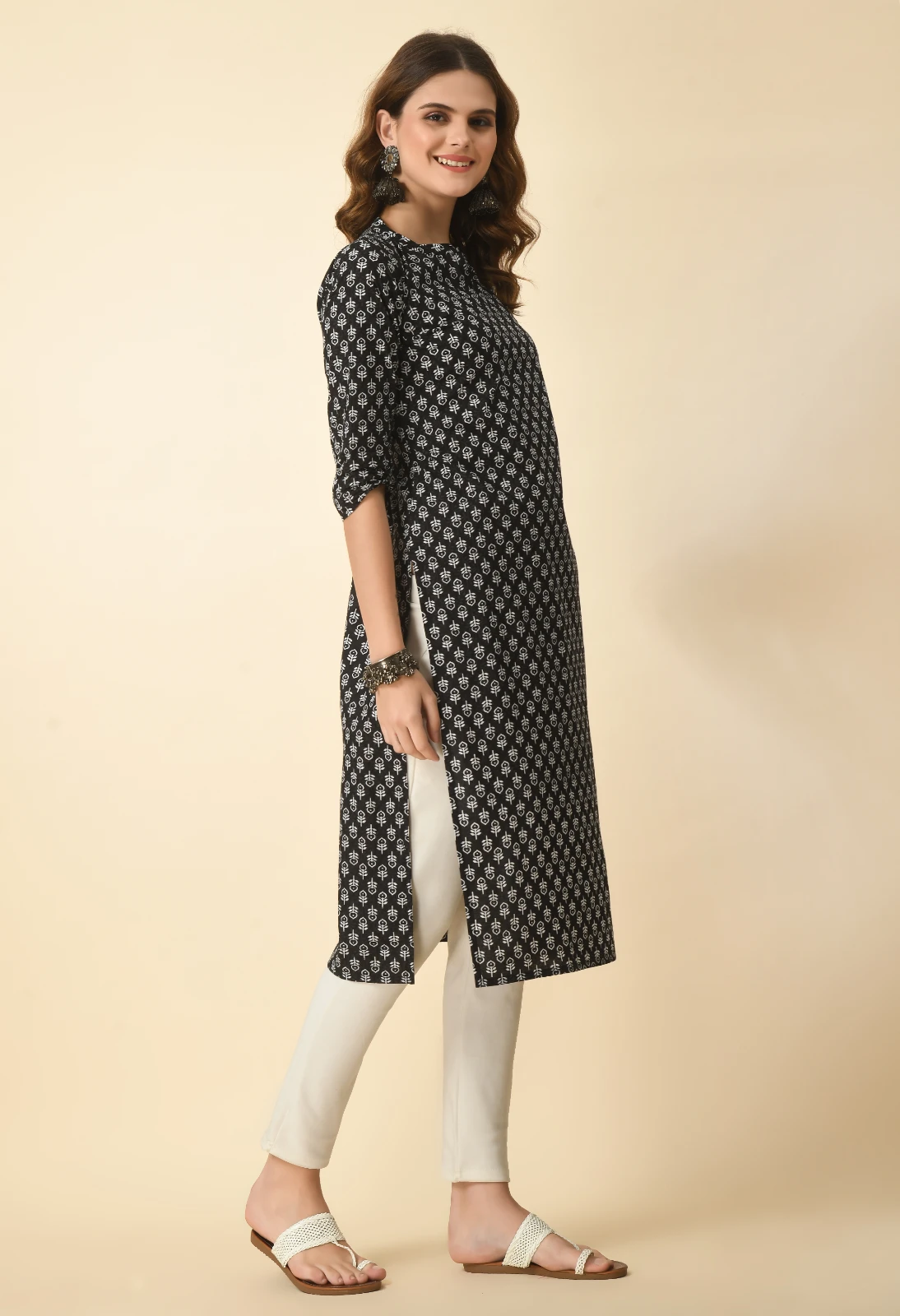 Three-quarter angled view of black printed kurta with side slit, worn with off-white pants and flats