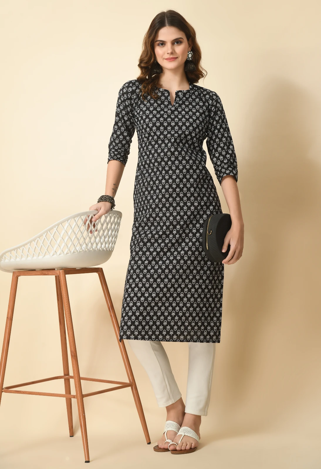 Full-length styled look with black printed kurta, off-white slim pants, white sandals and a round black clutch