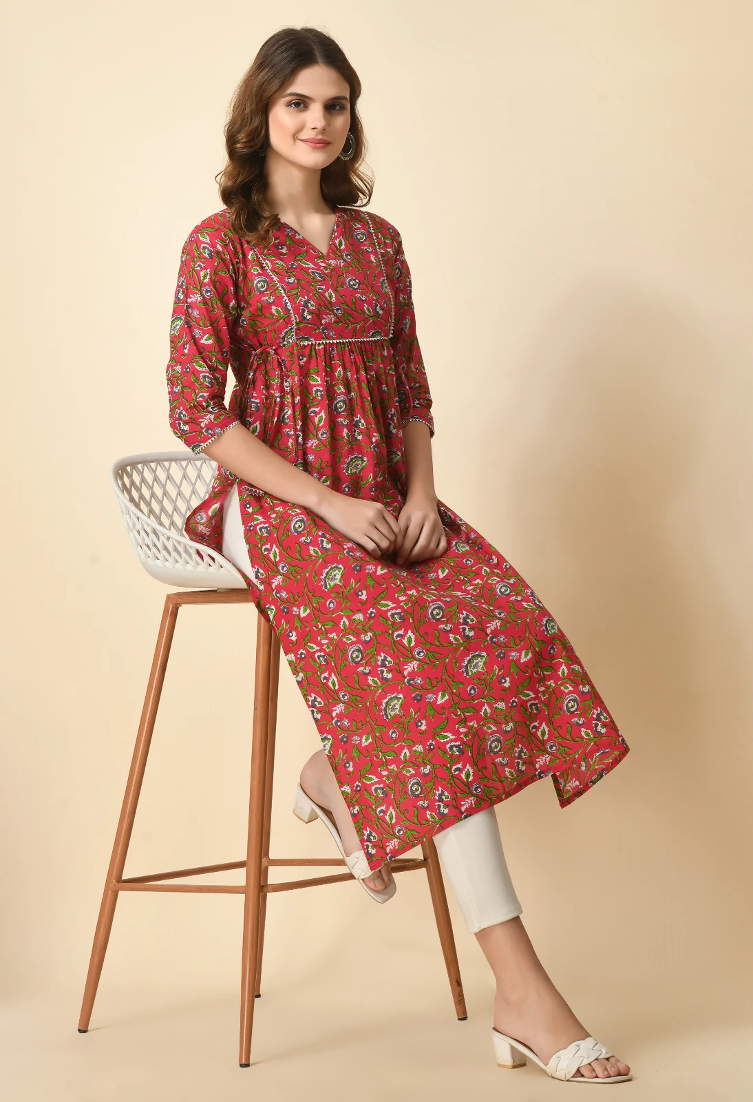 Seated view of the red printed kurta on a tall chair, showing the drape and front slit