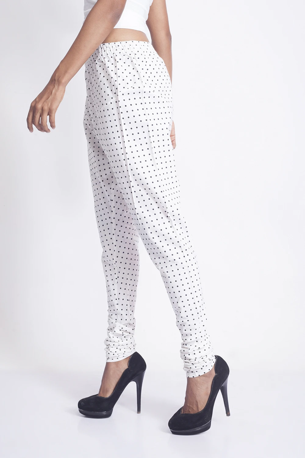 Side view of white polka dot slim fit pants with a gathered waist and ruched ankles, styled with black heels