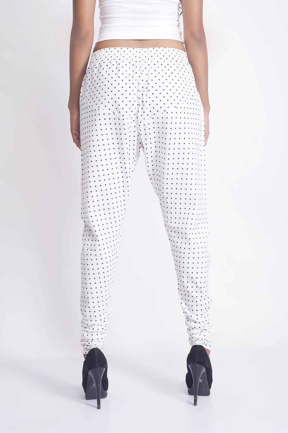 Back view of white polka dot slim fit pants with an elastic waistband and slim ruched legs above black heels