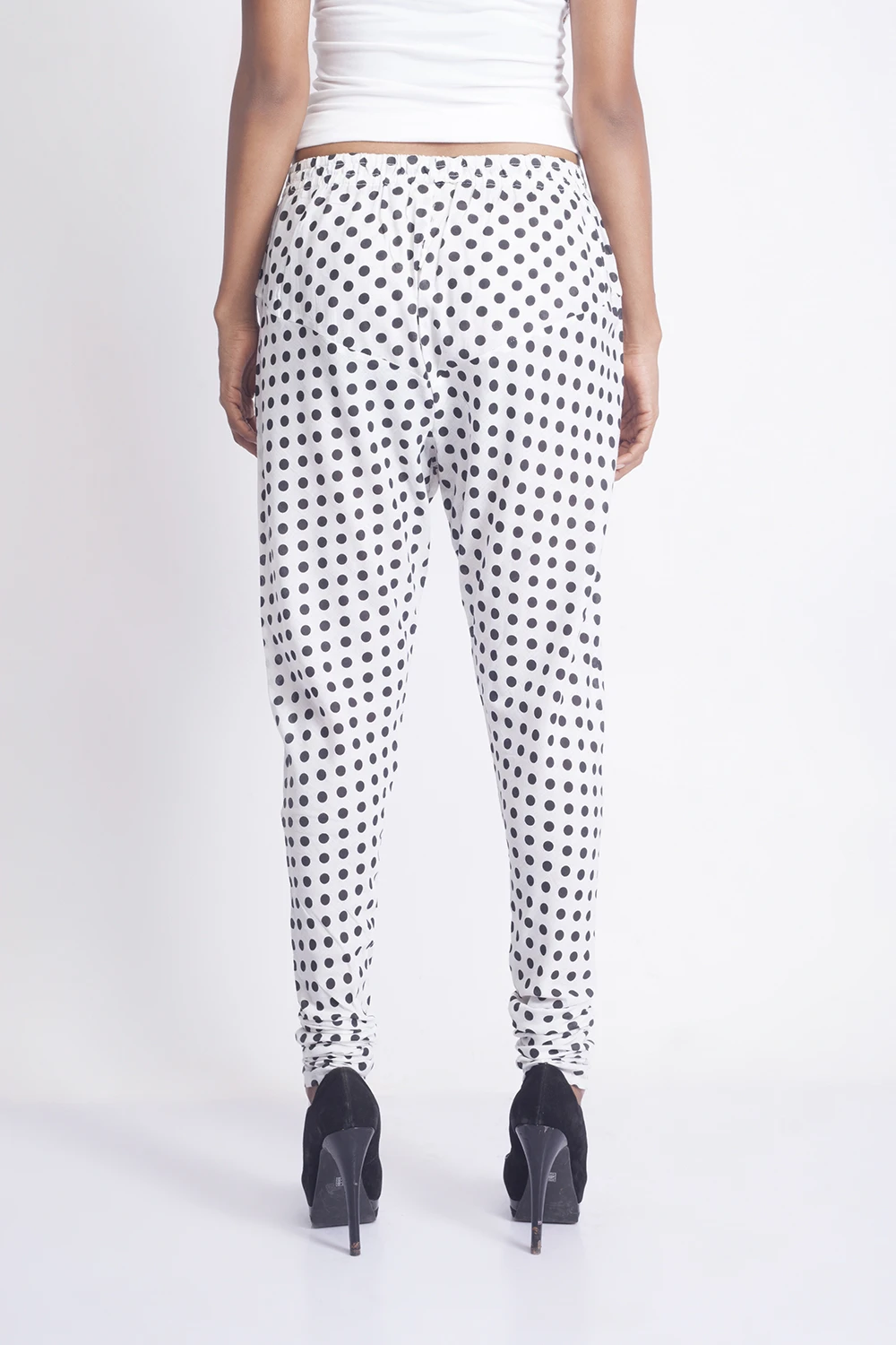 Back view of white polka dot leggings with a gathered waistband and stacked hems, worn with black heels