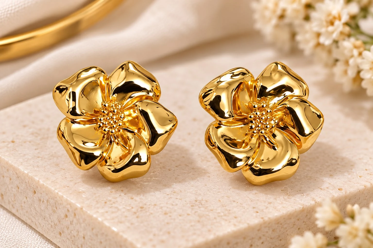 Pair of glossy gold-tone flower stud earrings displayed on a beige stone block
