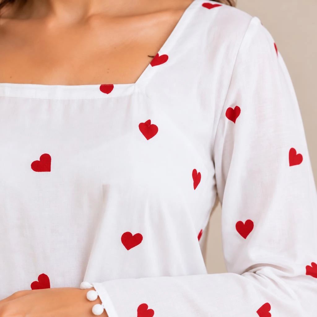 Close-up of square neckline, red heart print and long sleeve cuff with white pom-pom trim