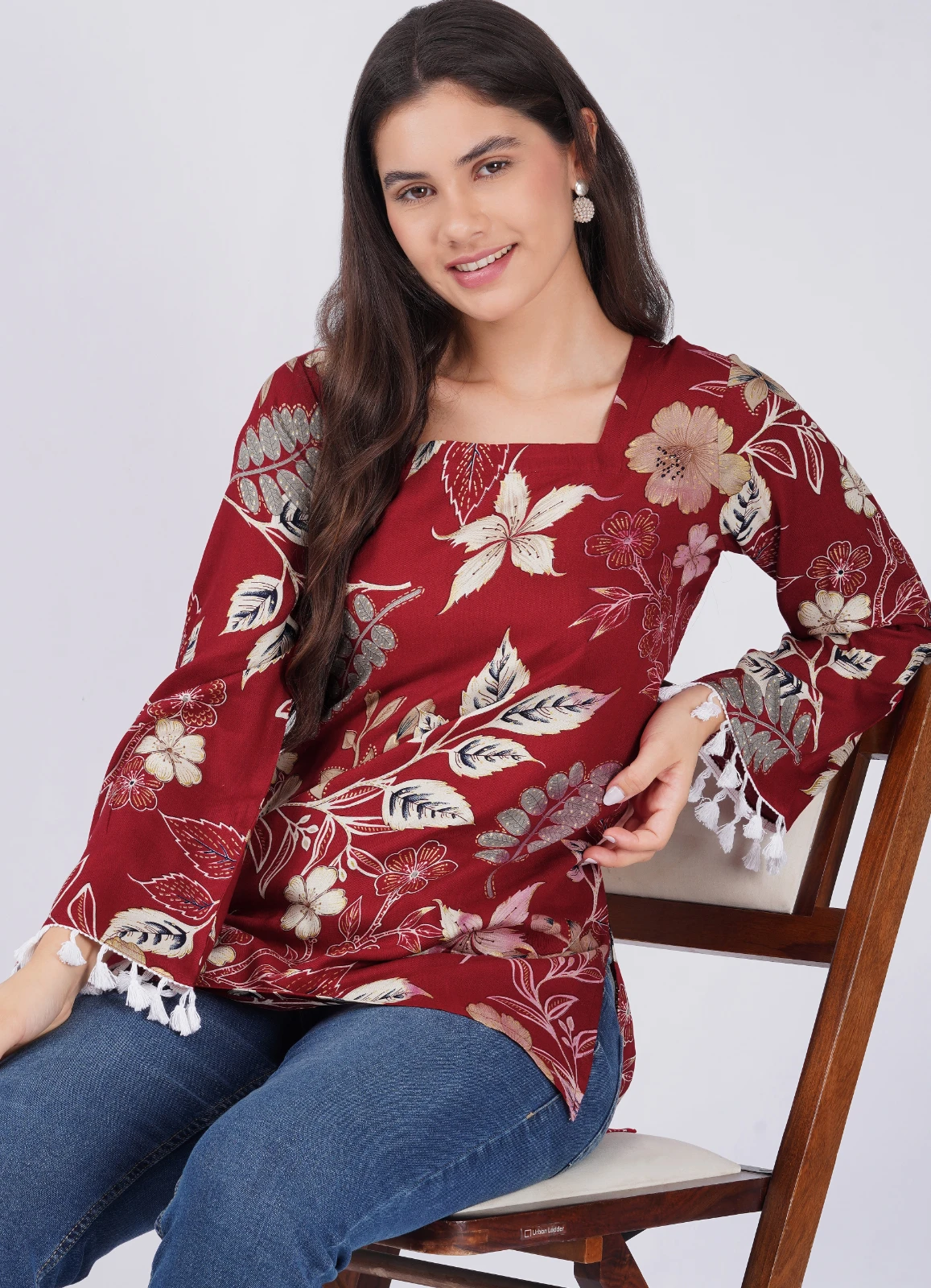 Seated styling view of the maroon floral top with tassel sleeve hems