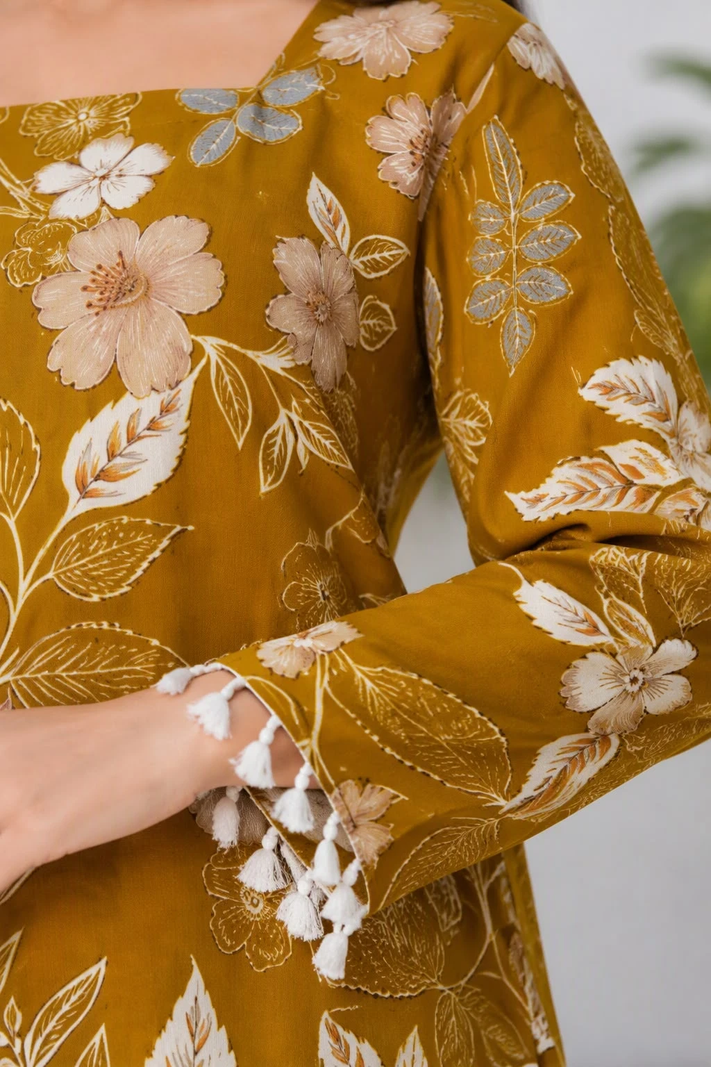 Close-up of floral print fabric, square neckline and white tassel trim on the sleeve cuff