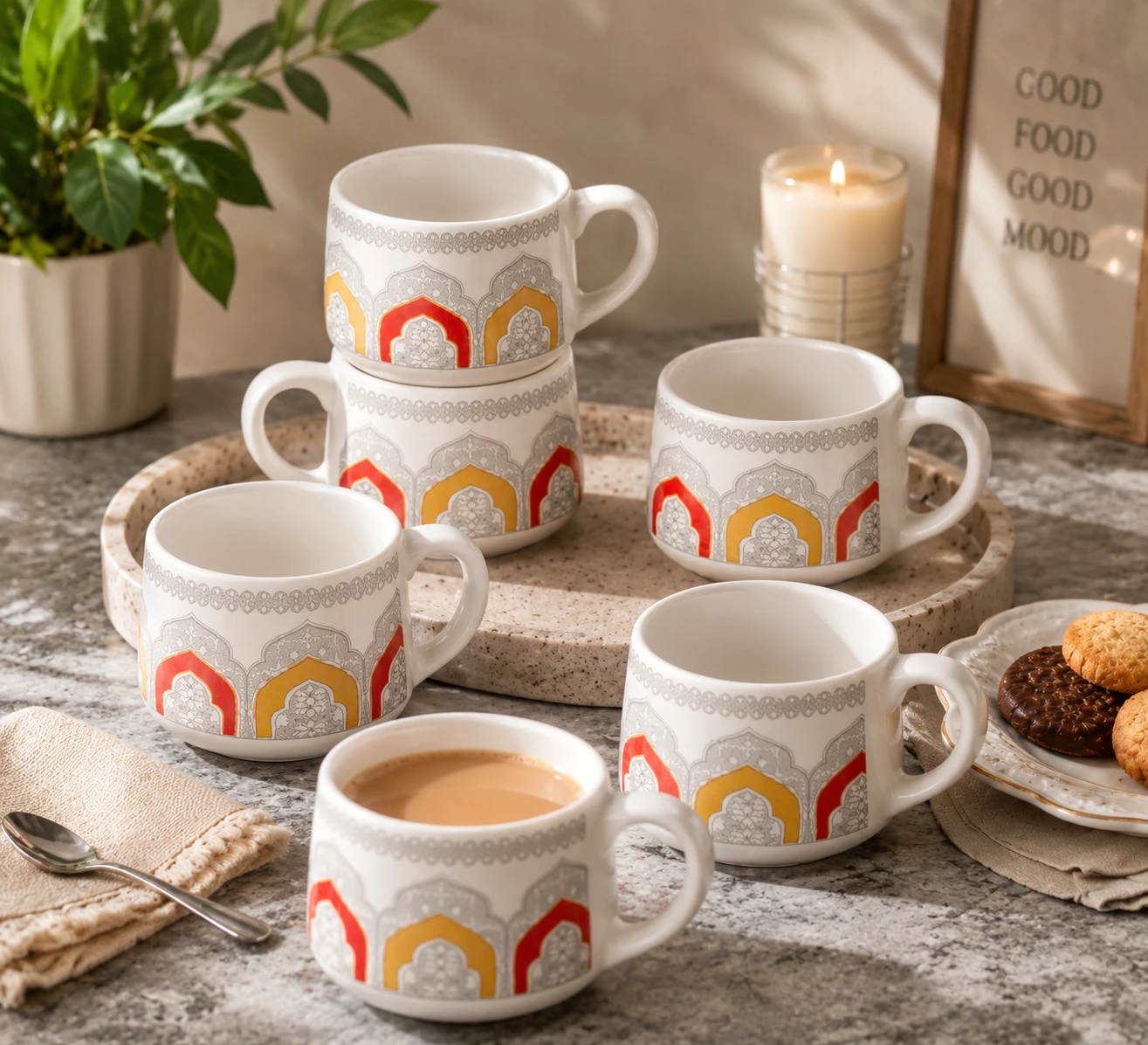 Six patterned ceramic mugs styled on a tray with cookies, candle and one mug filled