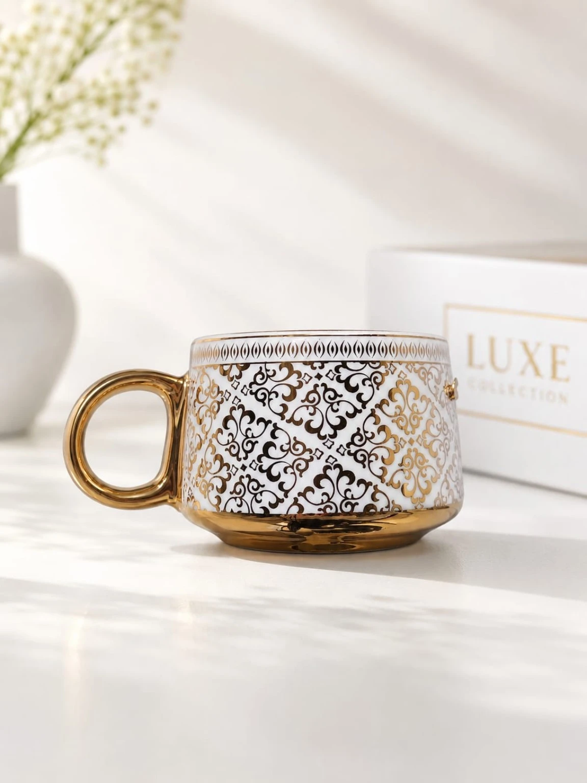 Single mug side view showing detailed gold-and-black scroll pattern and metallic gold base and handle