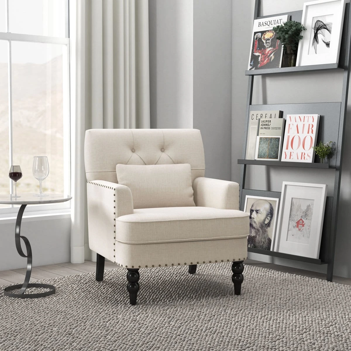 Cream accent chair styled in a living room beside a ladder shelf, showing front-left angle and nailhead trim