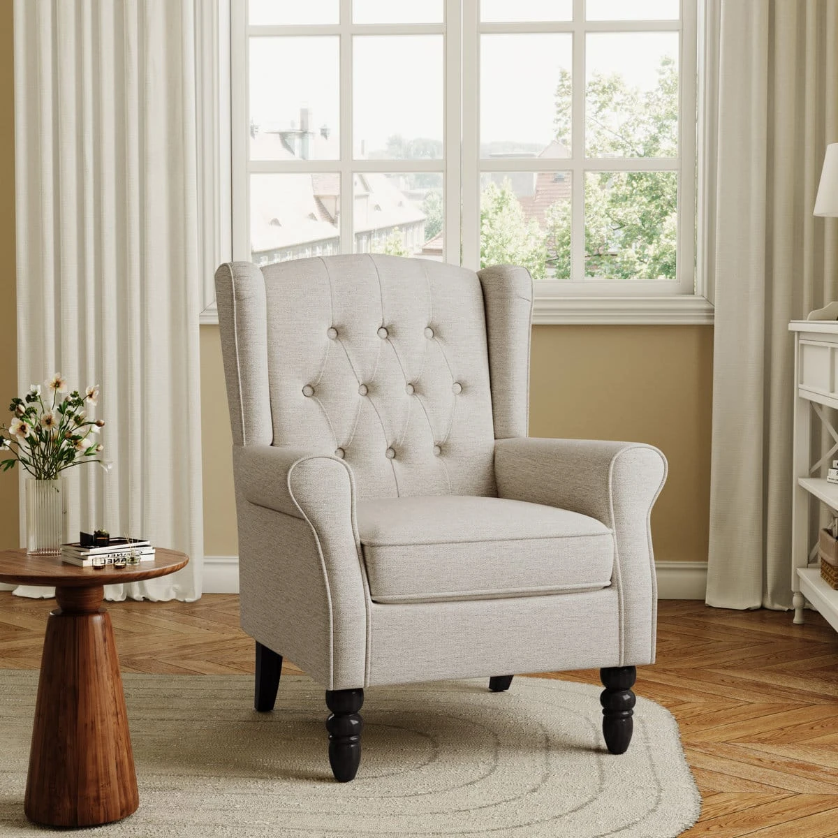 Alternate room view of a light beige wingback-style tufted chair with rolled arms and dark turned front legs
