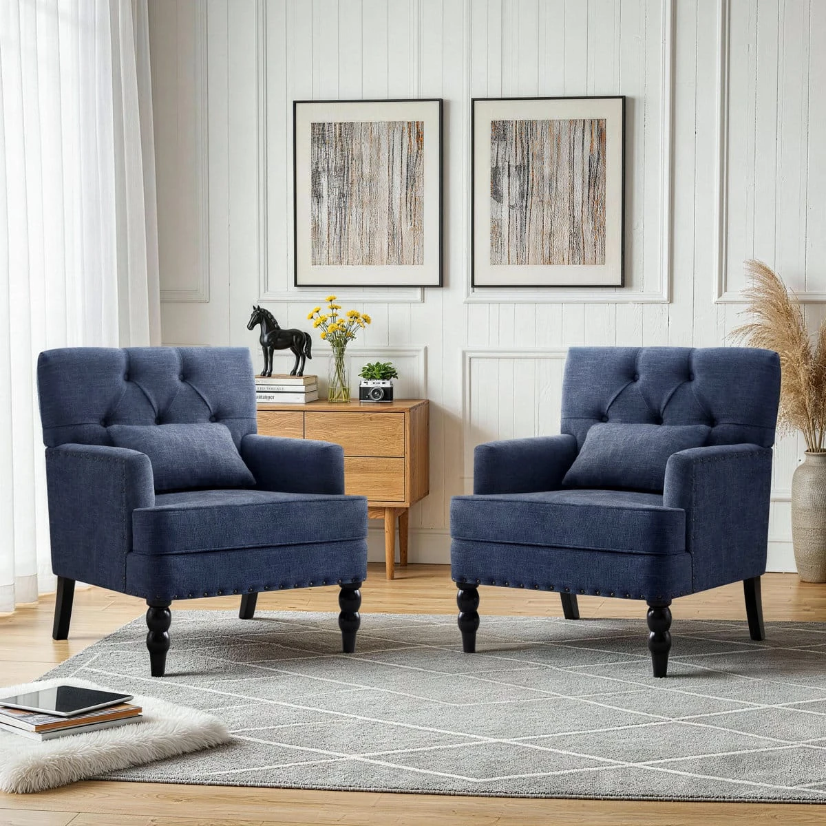 Two matching blue tufted accent chairs displayed together on a rug in a bright sitting room