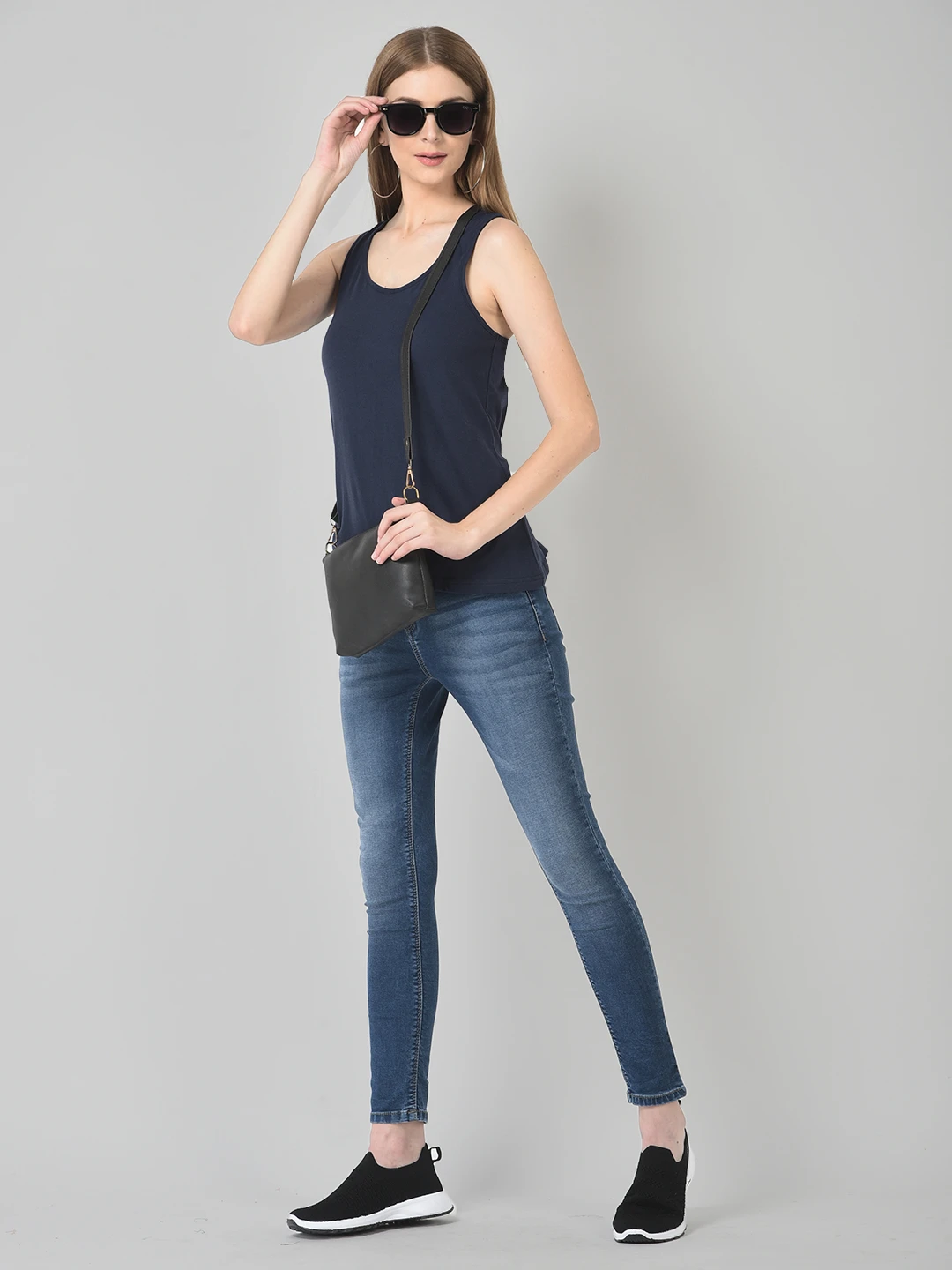 Full-length styled look with the navy tank top paired with jeans, sneakers and crossbody bag