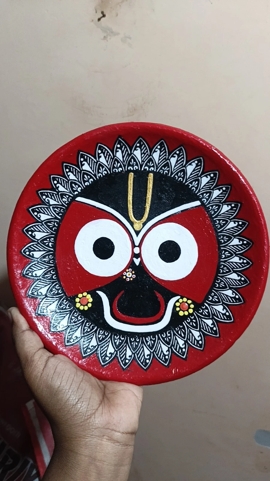 Close front view held in hand, showing the glossy painted Jagannath design on the circular red plate