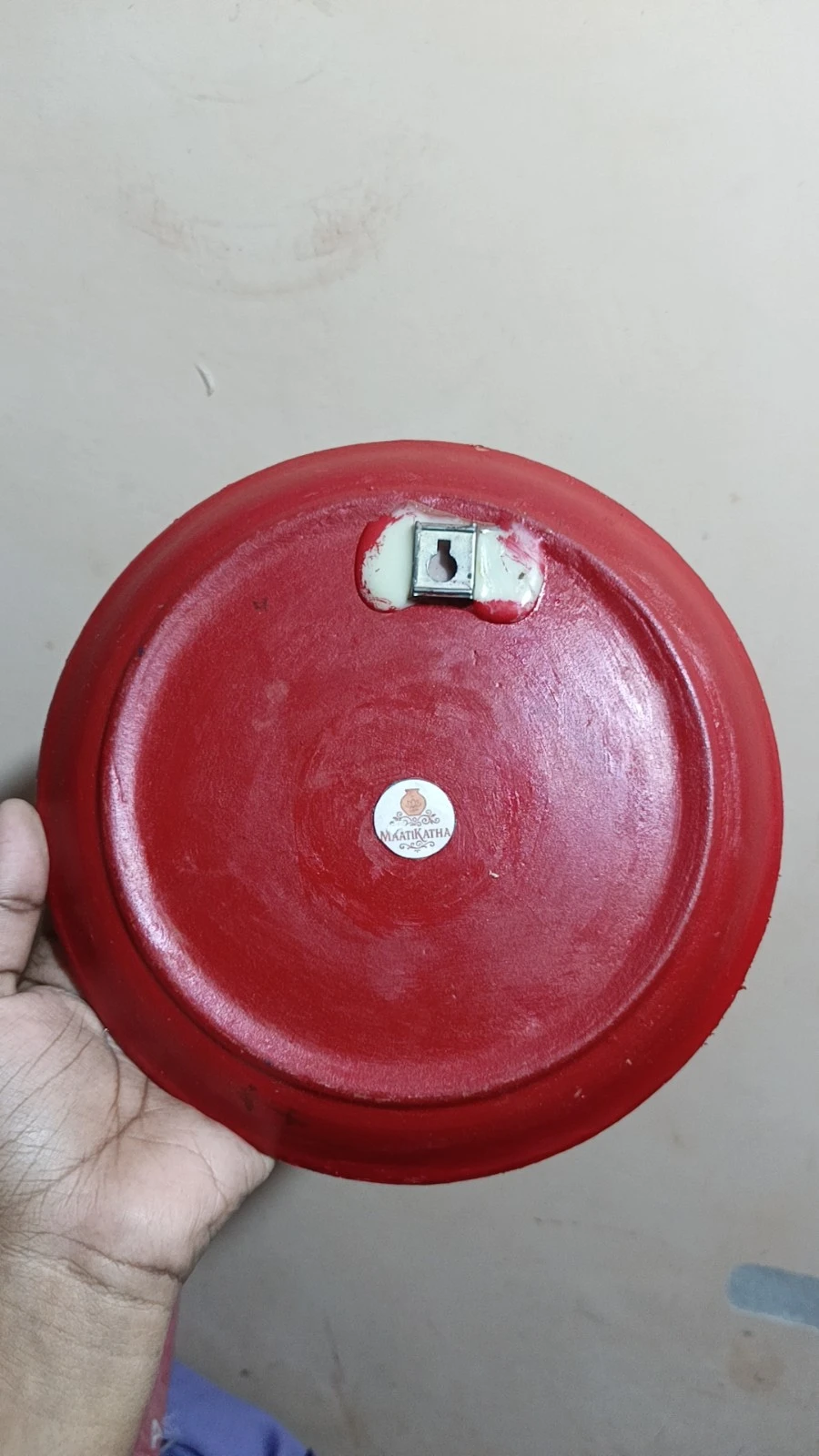 Back view of the red decorative plate with wall hook and Maatikatha brand sticker at the center