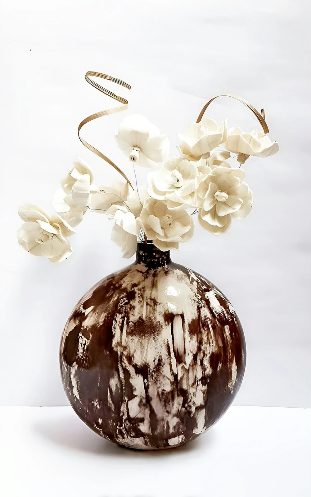 Vase displayed with cream artificial flowers against a plain white background