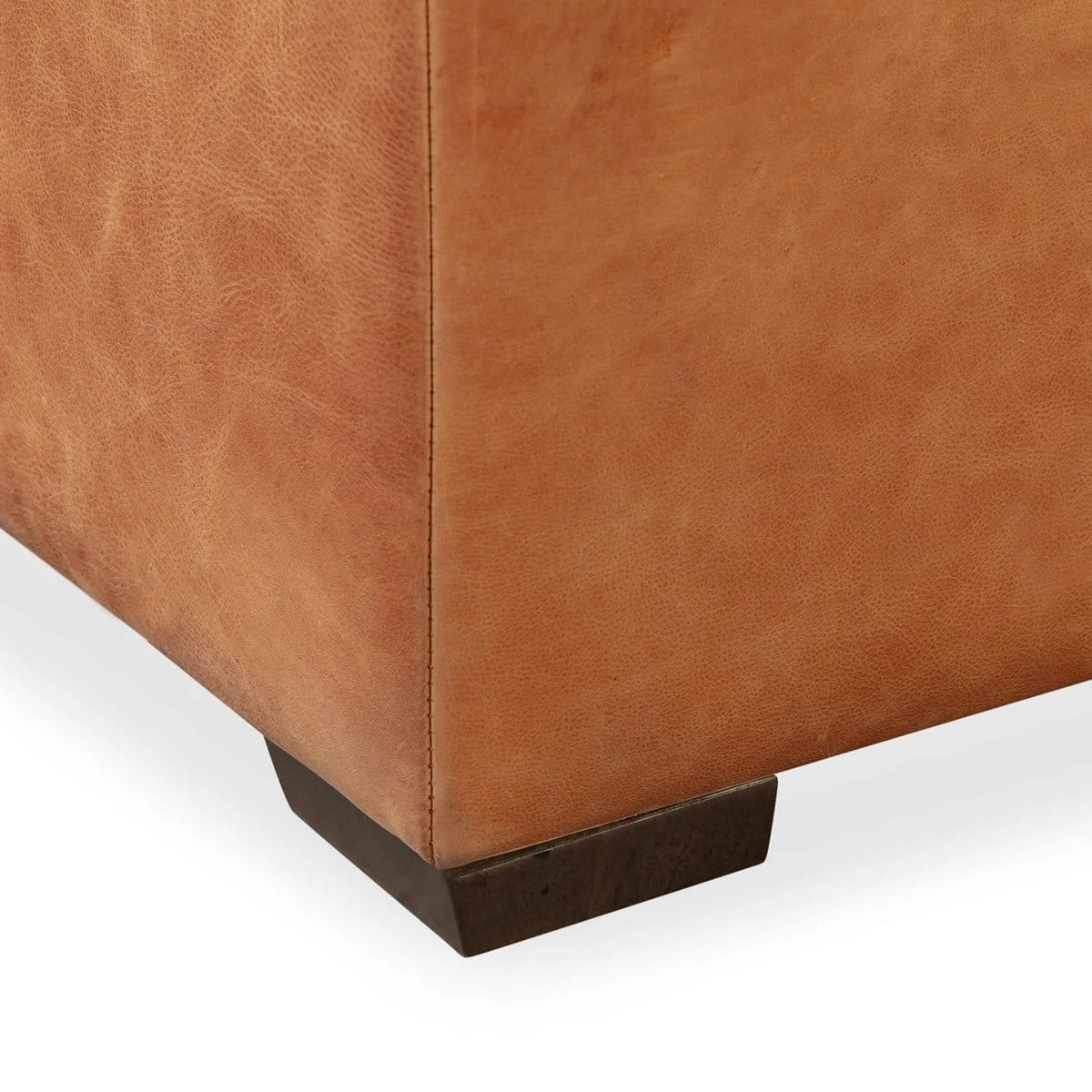 Detail of lower corner seam and dark wood block foot under cognac leather panel
