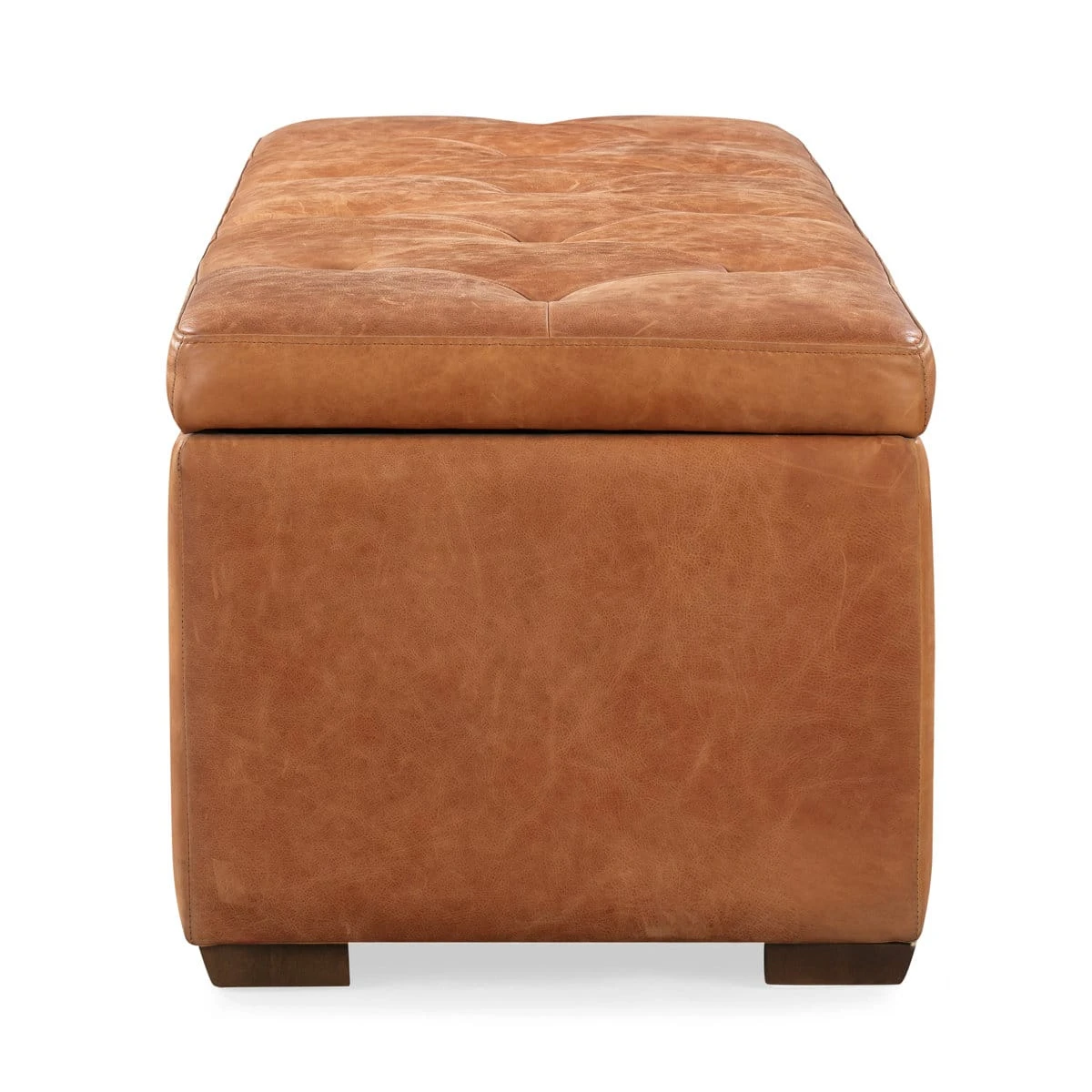 End view of the leather storage ottoman showing padded tufted lid and two wood feet