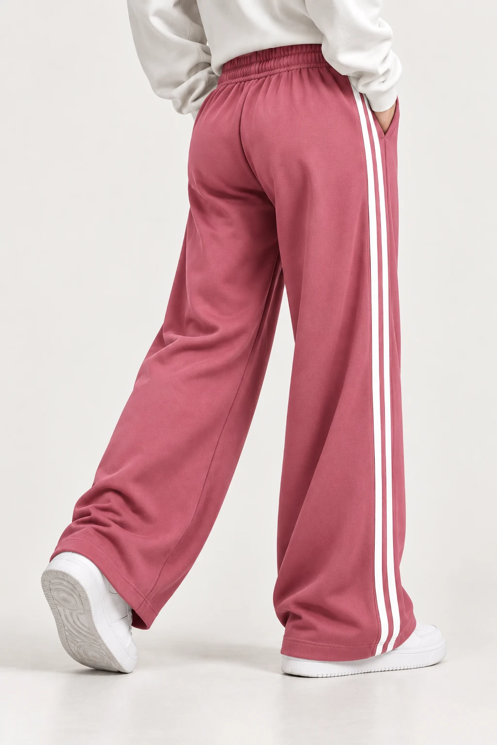 Back three-quarter view of dusty pink wide-leg track pants with elastic waist and white side stripes