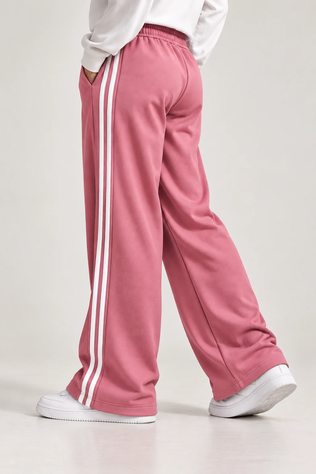 Side-back angle showing pink track pants drape, pocket opening, and double white stripes to the hem