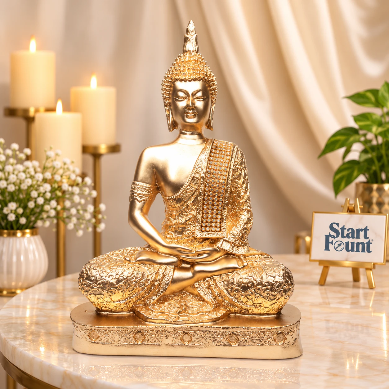 Gold meditating Buddha idol styled on marble table with candles, flowers, and Start Fount sign