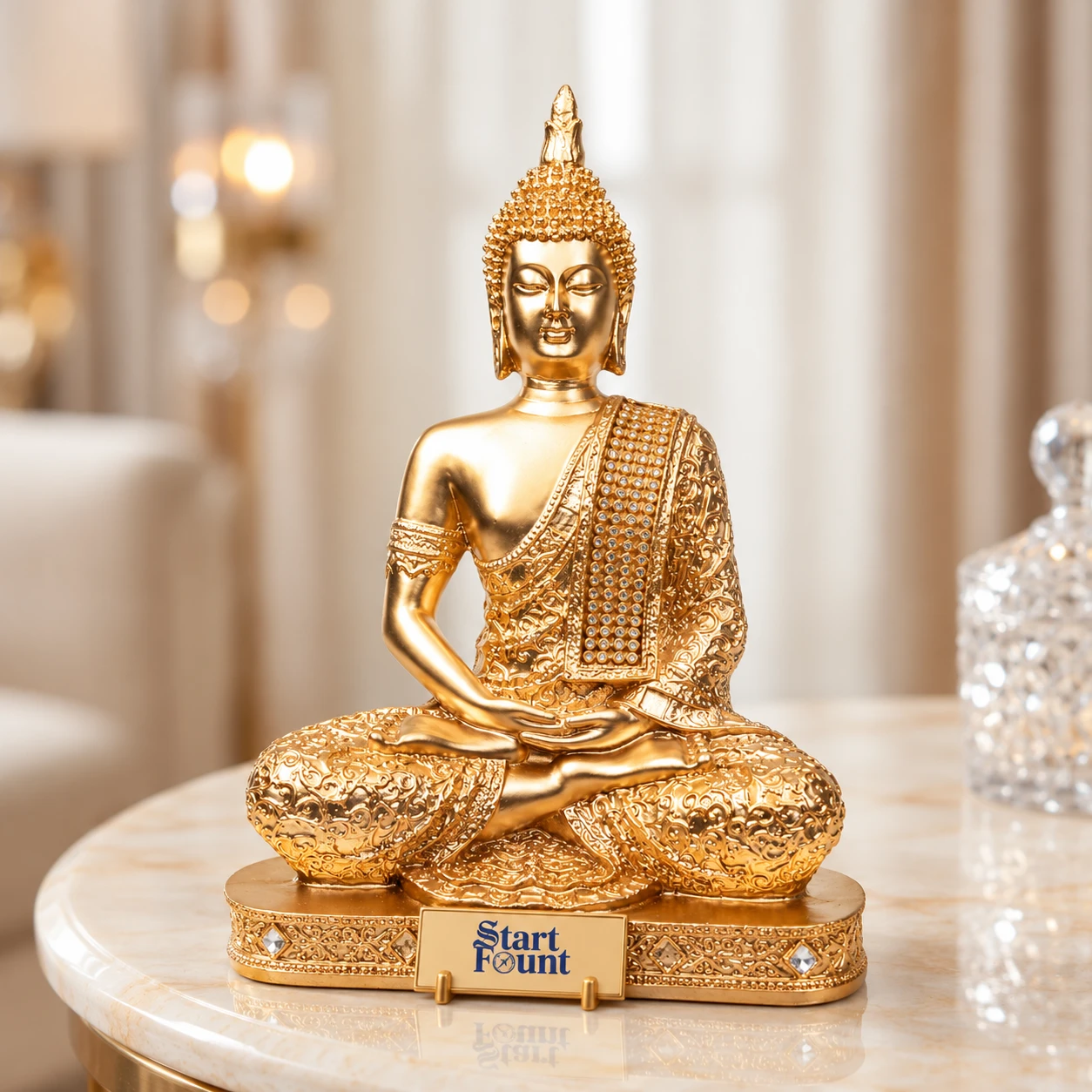 Front view of gold Buddha statue with ornate robe and jeweled drape on a decorative base