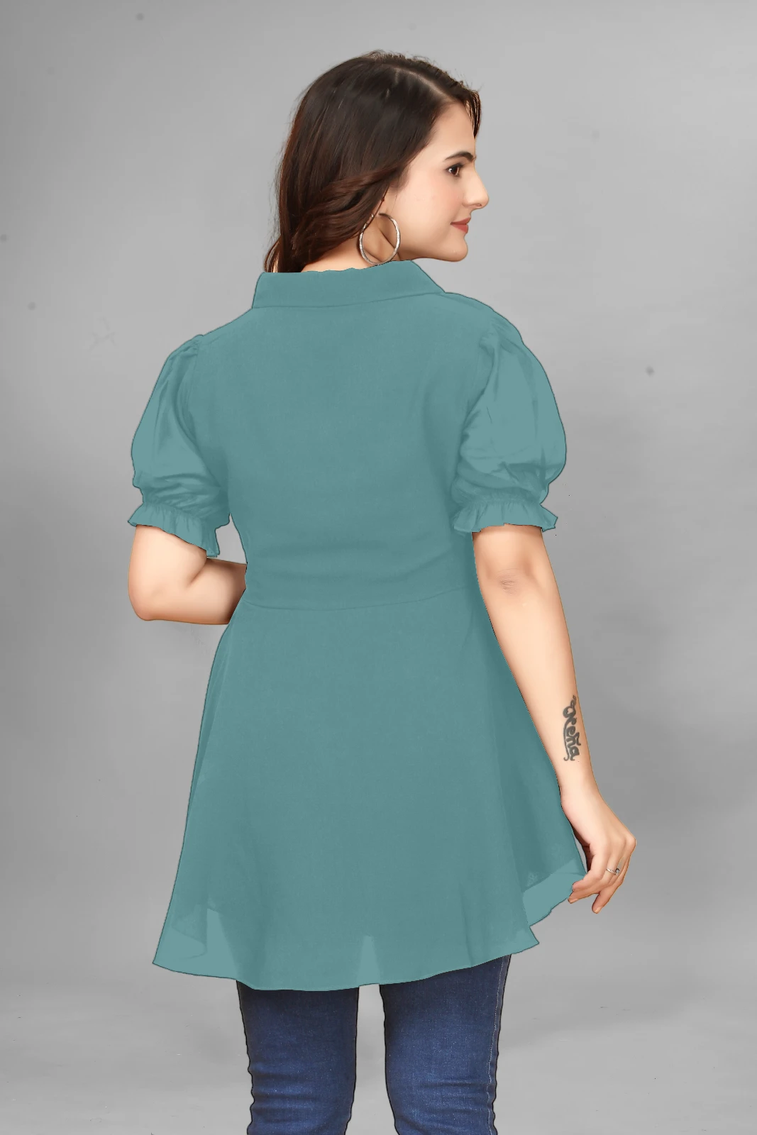 Woman wearing a teal peplum top with puff sleeves, dark jeans, hoop earrings and black sunglasses