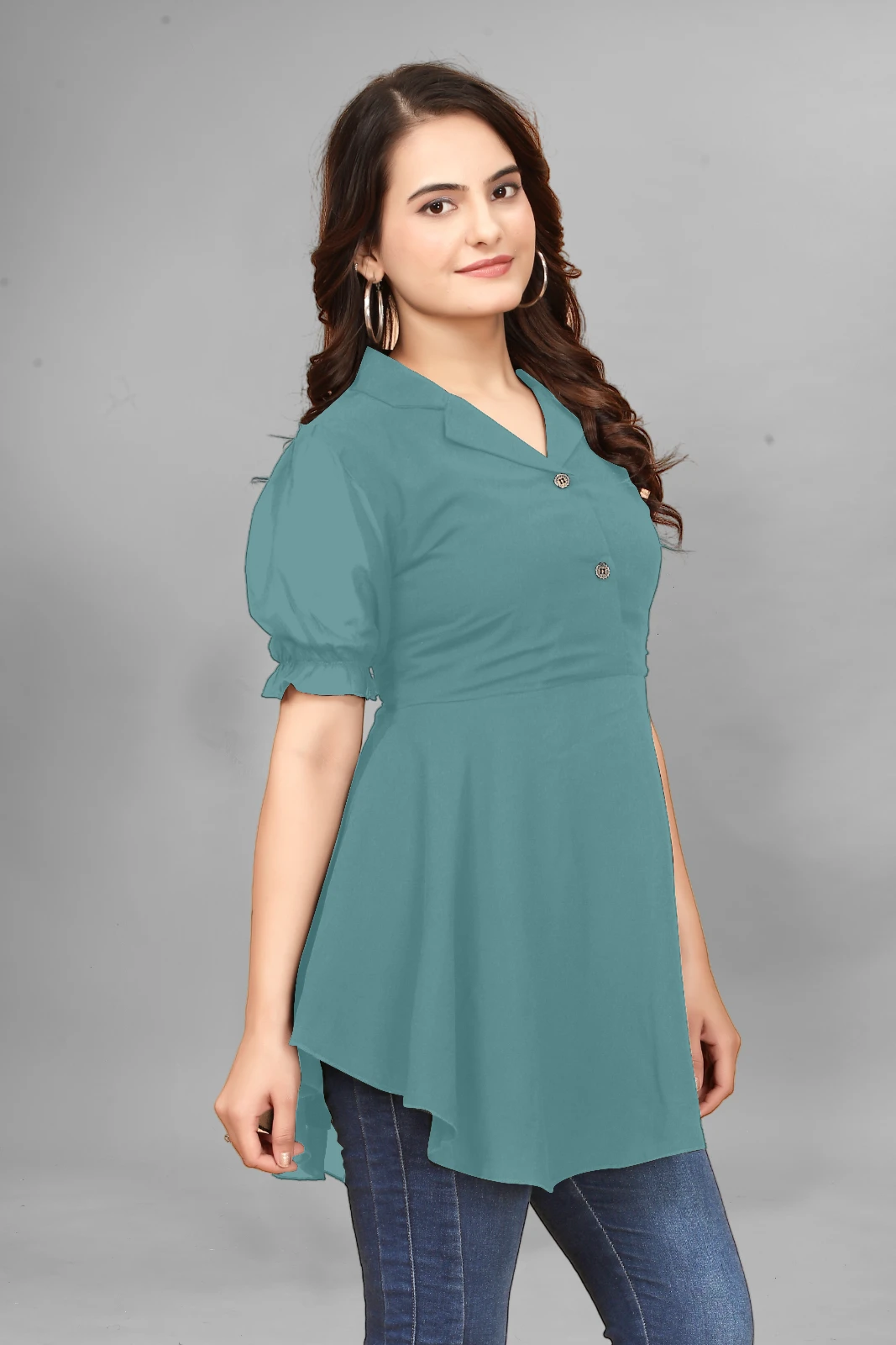 Woman wearing a teal peplum top with puff sleeves, dark jeans, hoop earrings and black sunglasses