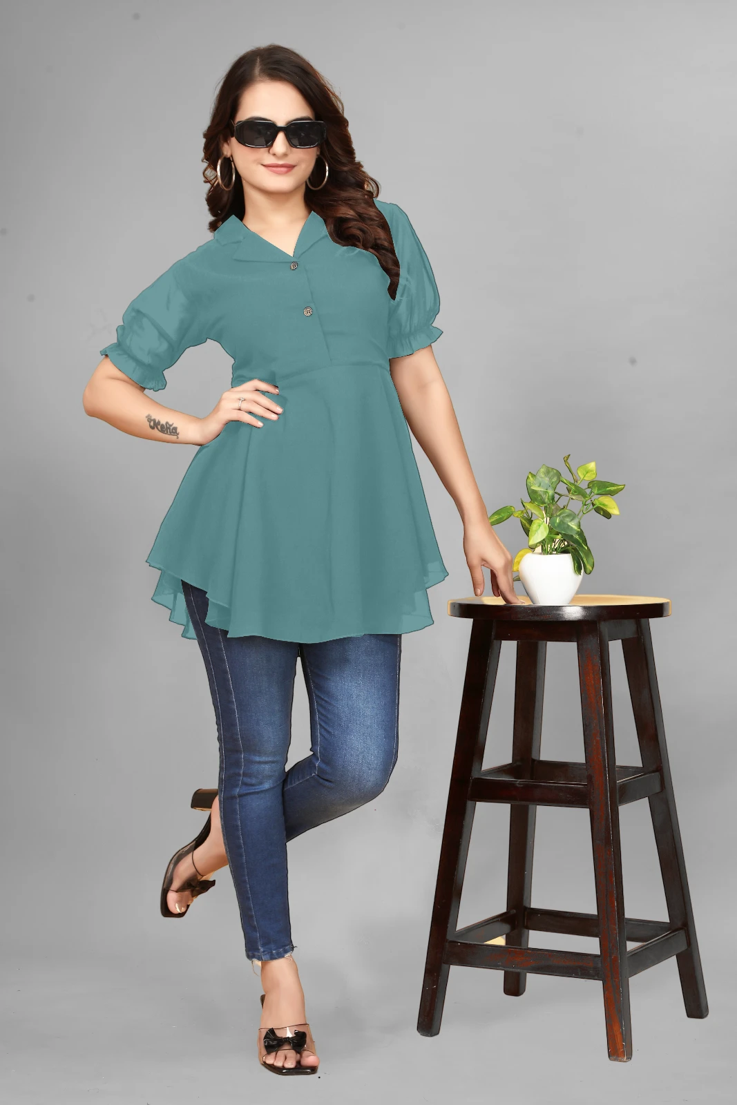 Woman wearing a teal peplum top with puff sleeves, dark jeans, hoop earrings and black sunglasses