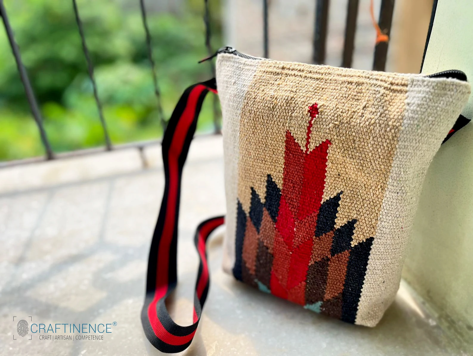 Handwoven geometric fabric shoulder bag with red, brown and black pattern and black-red striped strap