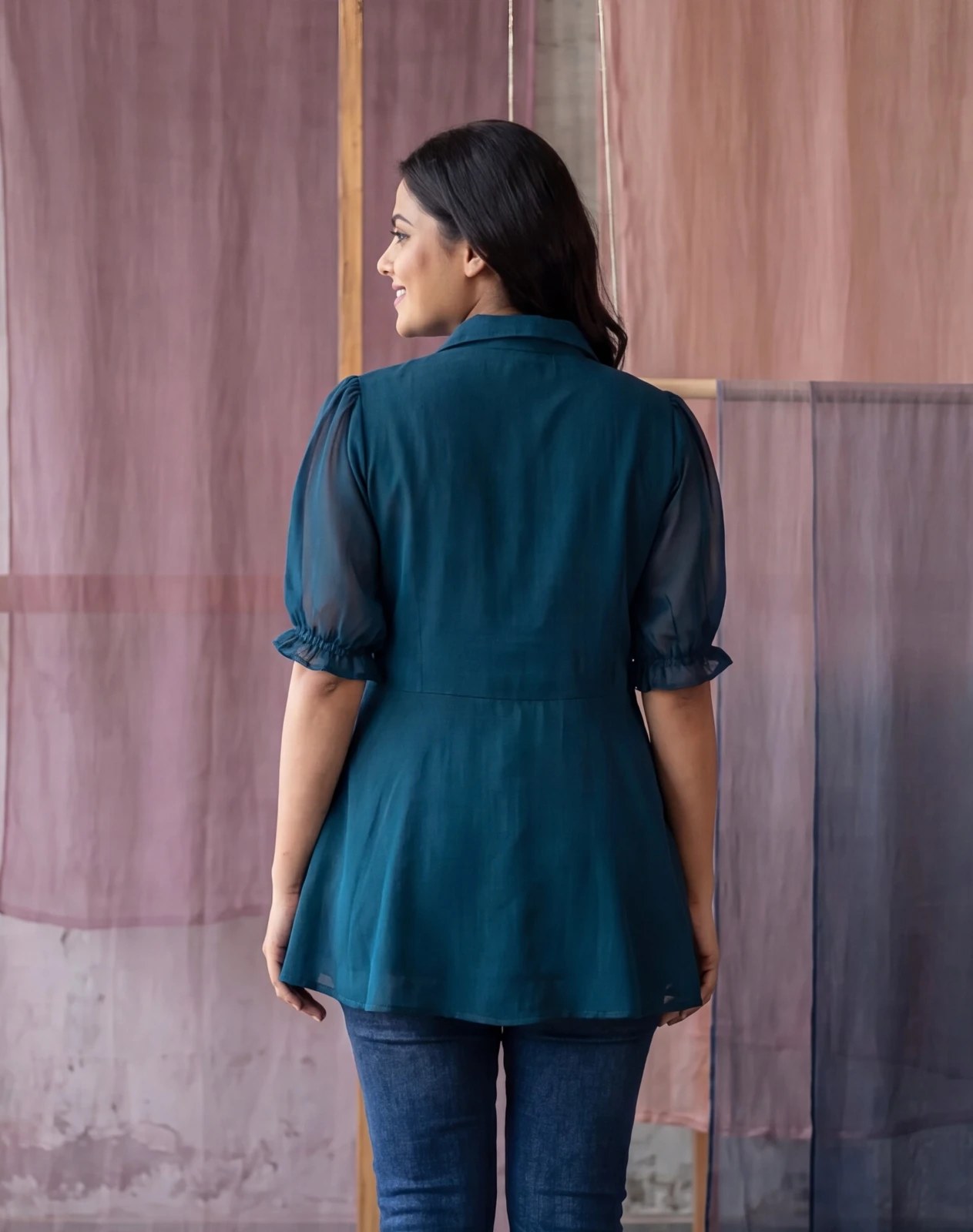 Woman wearing a teal collared tunic top with sheer puff sleeves and button detail over blue jeans