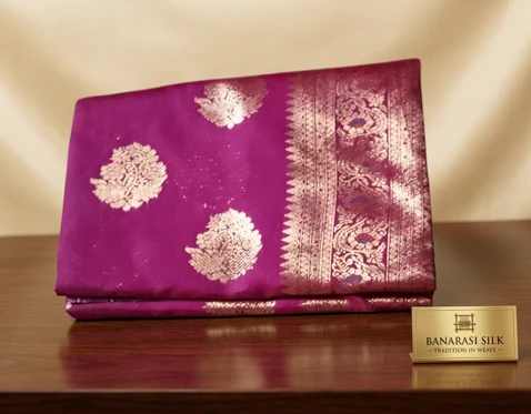 Woman wearing a bright pink silk saree with gold zari motifs and border, paired with a golden blouse