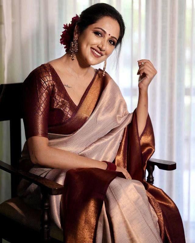 Woman wearing a beige silk saree with maroon border and matching blouse, styled with traditional jewelry