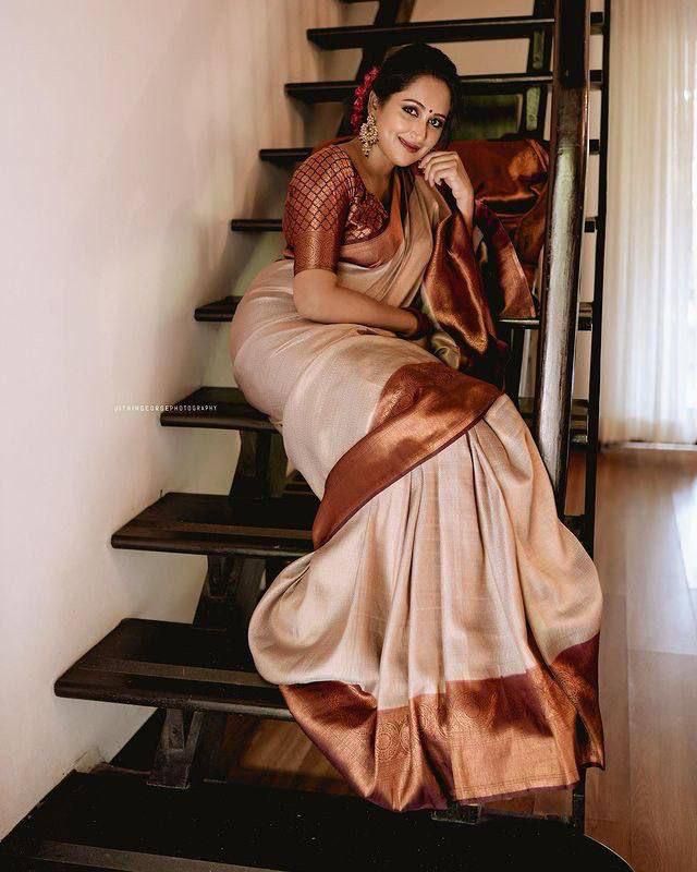 Woman wearing a beige silk saree with maroon border and matching blouse, styled with traditional jewelry