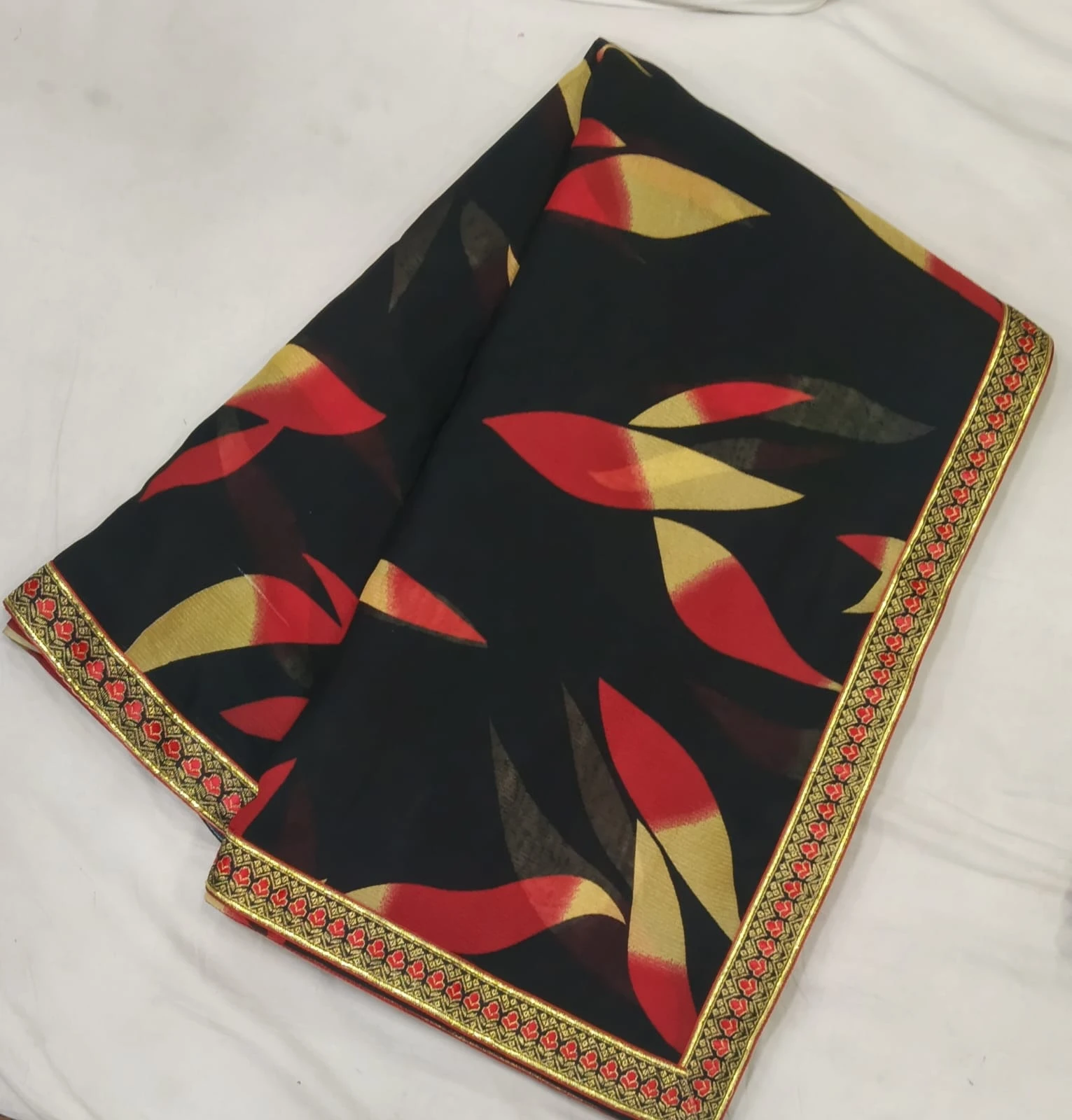 Folded black saree with red and beige abstract print and ornate red-gold border