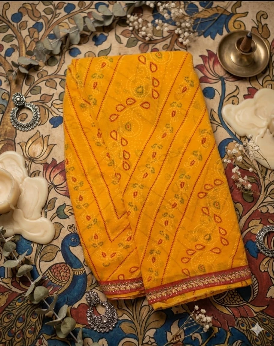 Folded yellow printed saree with red embellished border placed on a patterned surface