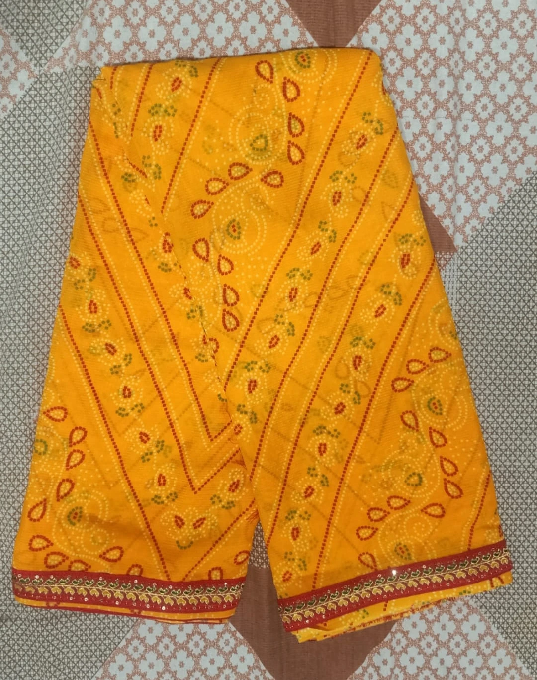 Folded yellow printed saree with red embellished border placed on a patterned surface