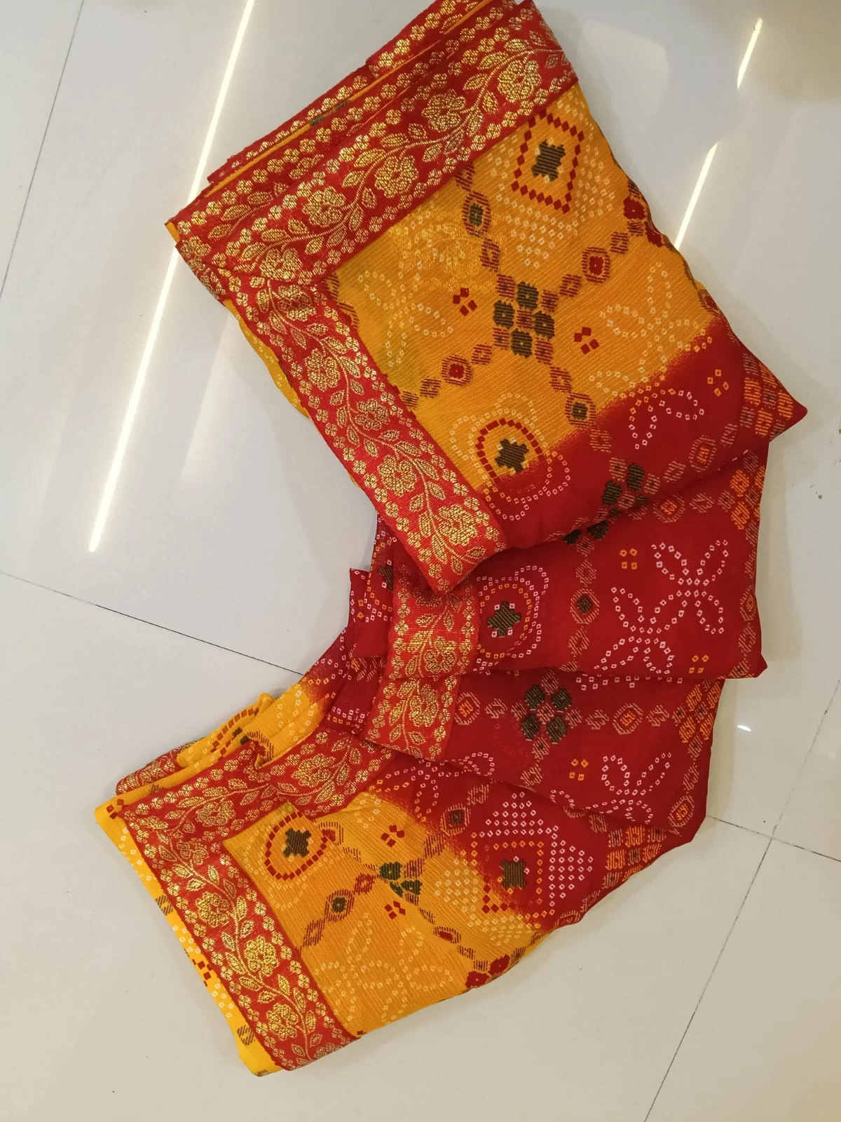 Folded red and yellow silk saree with gold floral border and traditional woven motifs