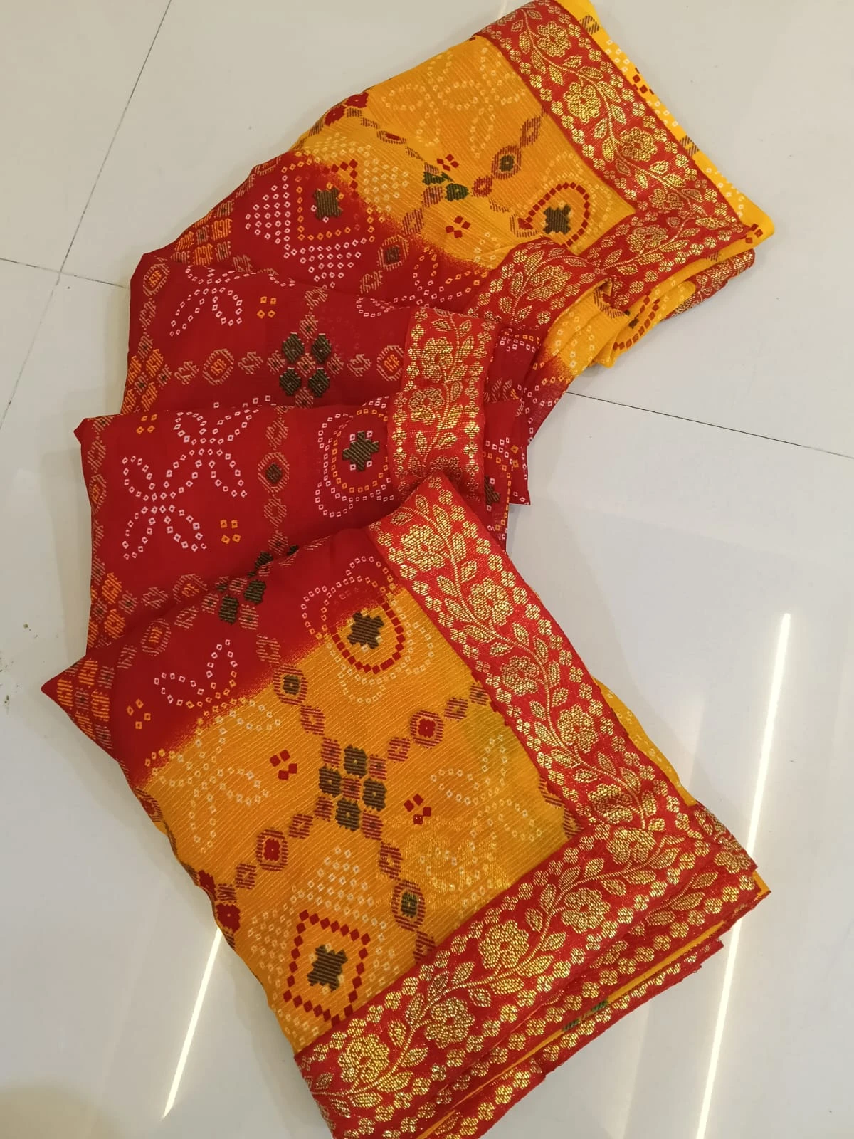 Folded red and yellow silk saree with gold floral border and traditional woven motifs